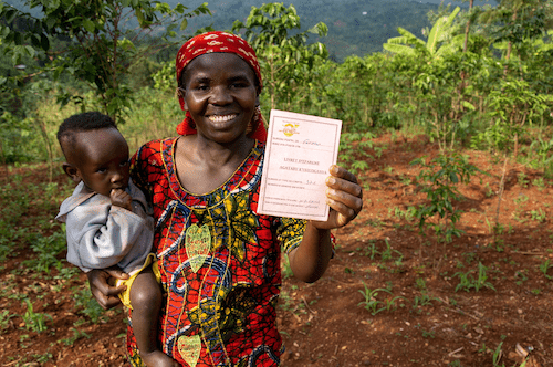 five talents case study showing a woman with a baby on her hip, proudly showing her certification as a successful business owner through their savings and loans model.